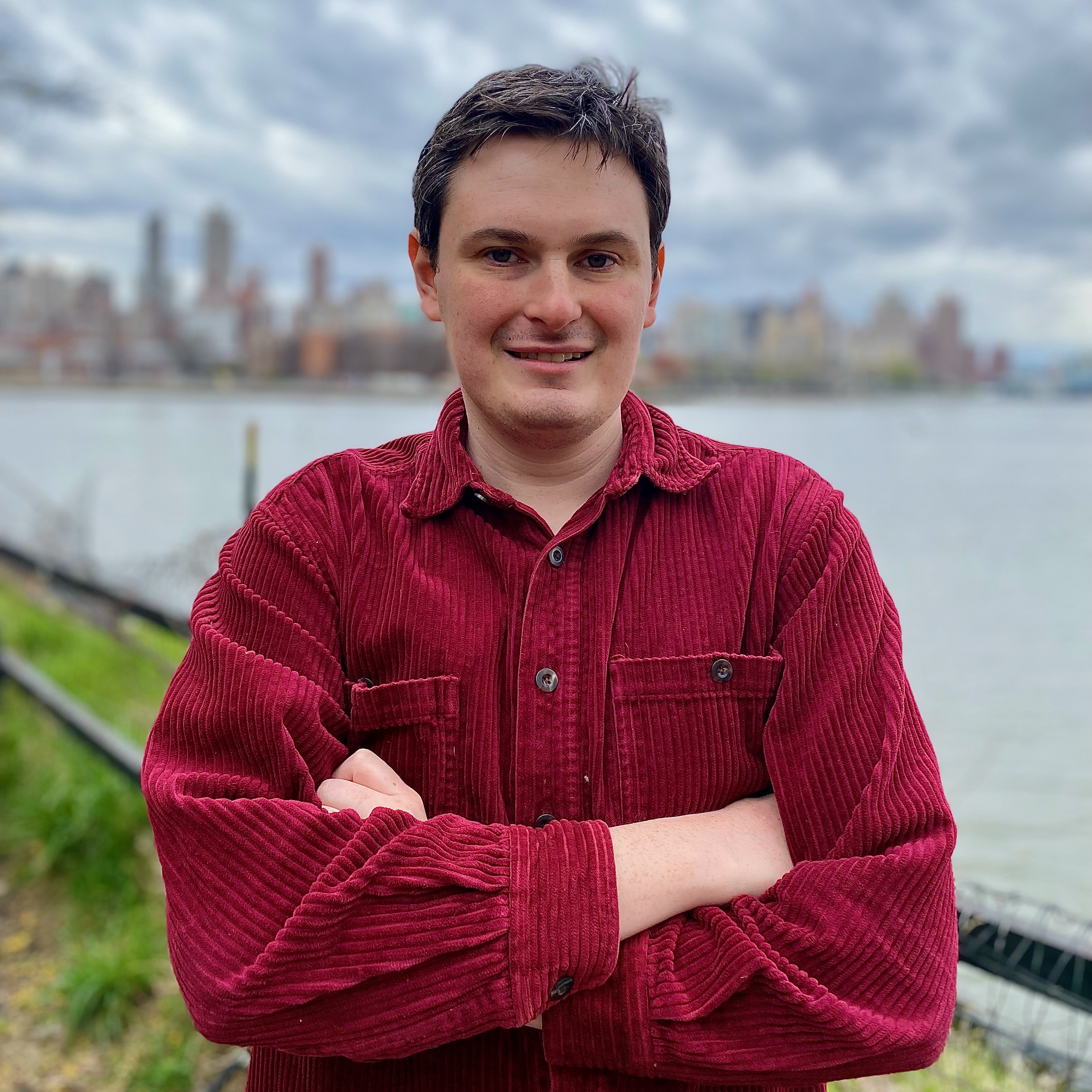 Dashiell Allen in a red shirt standing in front of the East River